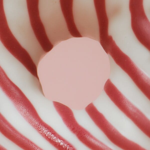 This image shows a red and white striped doughnut with a large hole in the middle, showing a soft pink background.