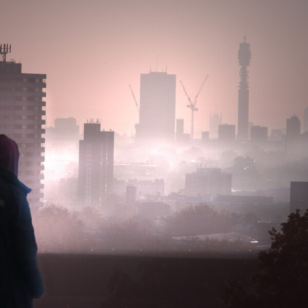A silhouette of a hooded individual overlooks a landscape of London shrouded in smog.