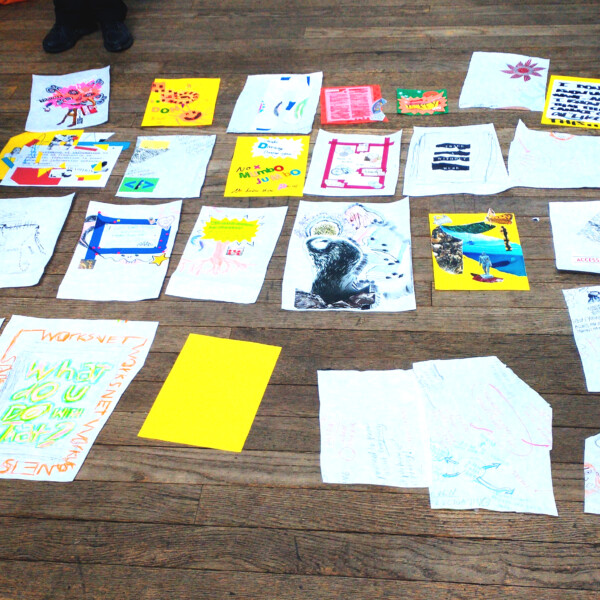 This image shows a person laying a grid of artworks on the floor in Conway hall.