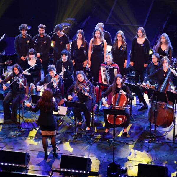 Members of the London Performing Academy of Music performing on stage. There is a variety of string instruments, woodwind, percussion and singers.