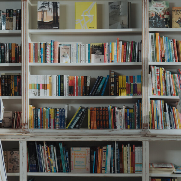 Two people are stood in front of full book shelves and reading a book in their hand.