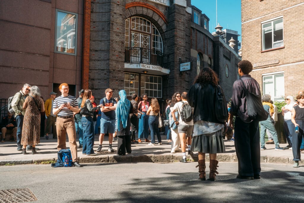 People walking and talking outside of Conway Hall in the sunshine.