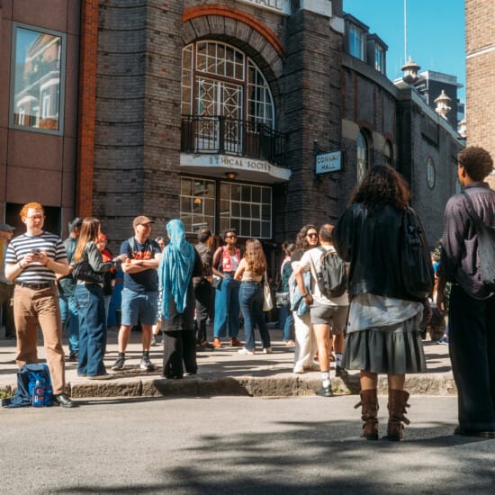People walking and talking outside of Conway Hall in the sunshine.